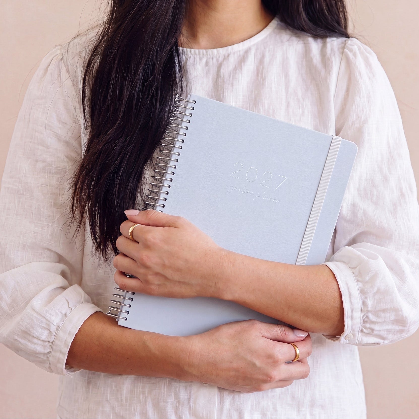 2027 Signature Planner in Dusk held by a woman in a white linen shirt, silver coil and cream elastic closure.