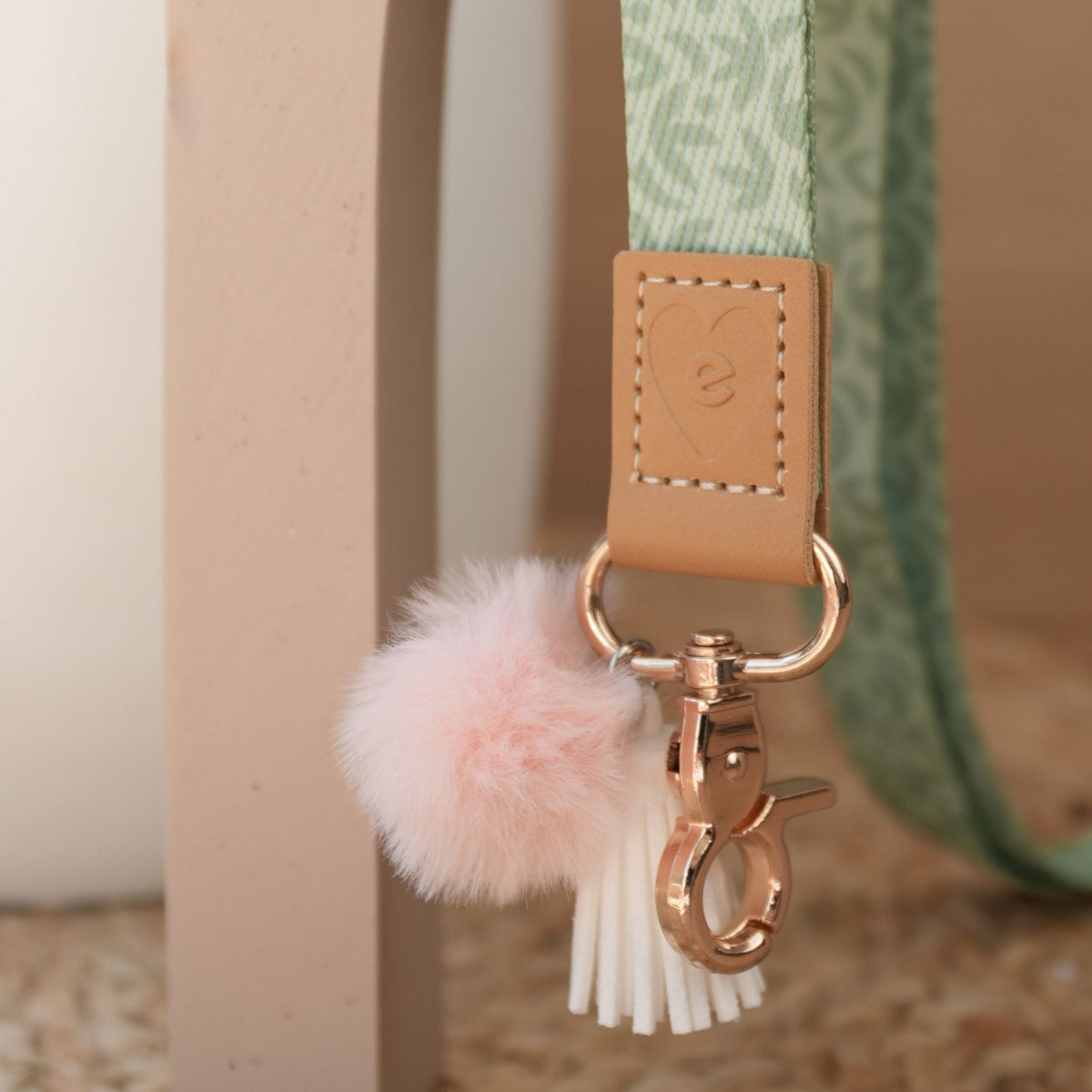 Close up of Sunburst Sage teacher lanyard, sage green print, gold clasp, peach pom pom and white tassel